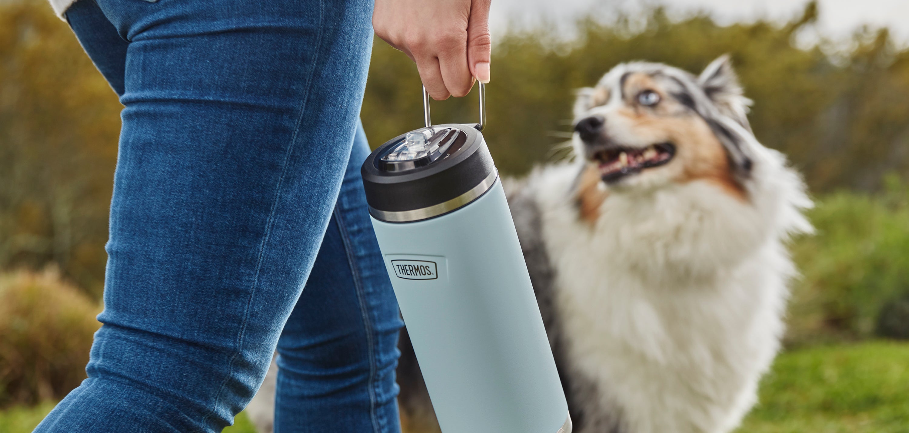 Person carrying a Thermos water bottle with their dog next to them.